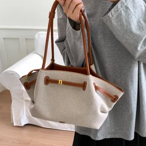 Detail of canvas tote bag with brown leather trim and golden logo on shoulder strap
