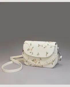 Detail der eleganten cremefarbenen Spitzentasche mit Blumenstickerei und Perlenkette