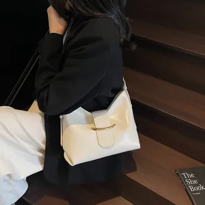 Detail of off-white leather crescent bag featuring a prominent gold curved metal buckle