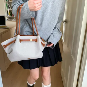 Detail of canvas tote bag with brown leather trim and metallic buckle on model