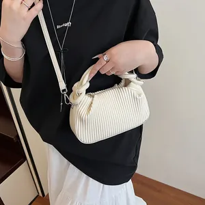 Gros plan du sac à bandoulière crème plissé verticalement avec poignée à nœud