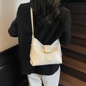 Modern cream shoulder bag with golden metallic buckle worn by model on stairs