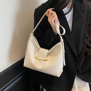 Close-up of minimalist cream leather bucket bag with elegant gold metal bar detail