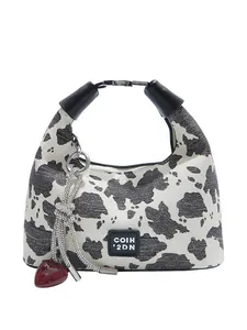 Cow print cross-body dumpling bag with heart charm and black handle on white background