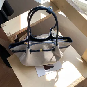 Detail of canvas tote bag showing navy leather trim and elegant golden metal buckle