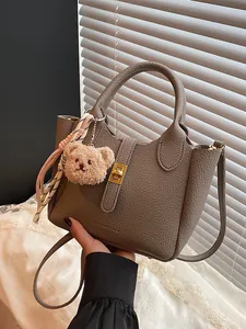 Sac seau en cuir beige foncé avec texture litchi, poignées et pendentif ours en peluche