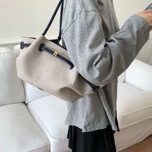 Detail of canvas tote bag with leather trim and gold metal lock on a white sofa