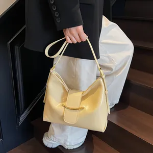 Close-up of cream yellow glossy leather shoulder bag with gold crescent metal bar