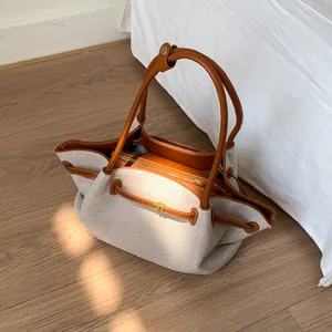 Detail shot of canvas tote bag featuring brown leather straps and gold metal zipper hardware