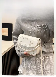 Detail einer weißen Tasche mit Blumenstickerei, Perlengriff und verstellbarem Riemen