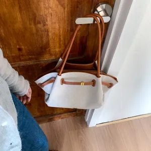Detail of white canvas tote bag with brown leather handles hanging on a wooden door