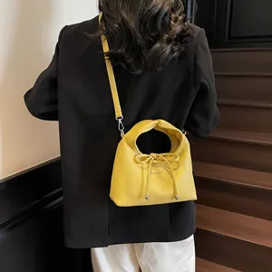 Detail of bright yellow leather handbag with twisted handle and bow charm on a model
