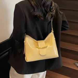 Close-up of a light yellow glossy leather shoulder bag with a gold crescent metal buckle