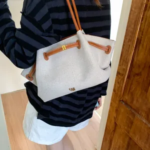 Detail of canvas tote bag with brown leather trim and metallic logo on beige fabric