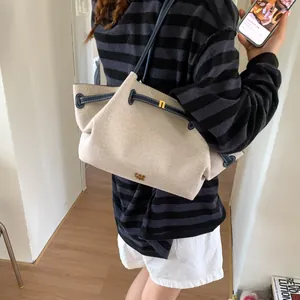 Detail of off-white canvas tote bag with dark blue leather trim and golden logo
