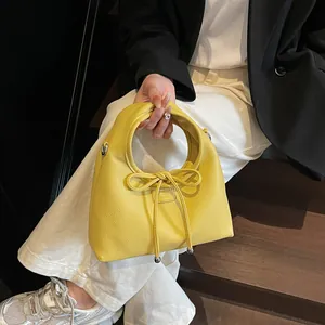 Detail of bright yellow lychee leather handbag with a large bow and metallic ball charms