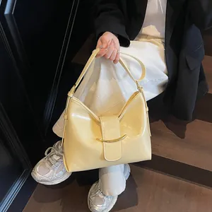 Detail of a creamy yellow bucket bag featuring glossy leather and a crescent gold clasp