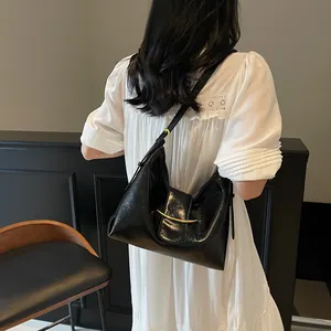 Detail of black glossy crescent bucket bag with gold buckle on white pleated dress