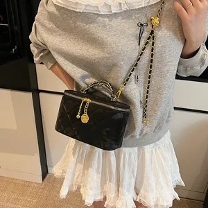 Détail du sac matelassé noir avec chaîne à boule dorée et doubles tirettes de zip