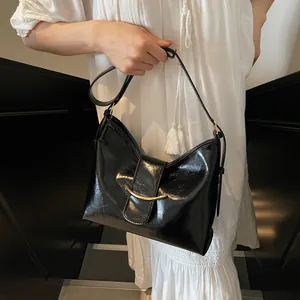 Detail of glossy black leather handbag with a minimalist golden curved metal buckle