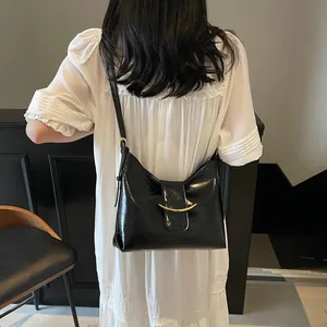 Detail of black patent leather bucket bag with gold buckle on a white dress