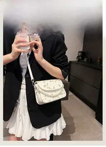 Detailansicht der weißen Spitzentasche mit gelber Stickerei und eleganter Perlenkette