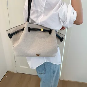 Detail of canvas tote bag with black leather straps and gold buckle worn by a model