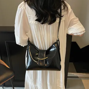 Detail of glossy black leather bucket bag featuring a crescent gold metallic buckle clasp