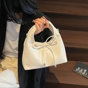 Detail of cream-colored lychee leather handbag featuring a stylish bow and metal beads