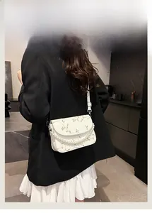 Detailaufnahme der eleganten weißen Spitzenstickerei und Perlenkette an der Umhängetasche