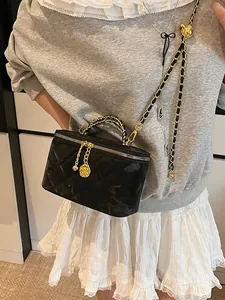 Sac boîte noir matelassé avec bandoulière chaîne dorée et breloque camélia sur modèle