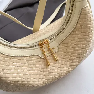 Detailed macro view of cream woven crescent bag with gold-tone dual zippers and texture