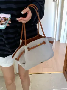 Large beige canvas tote bag with brown leather trim shown on shoulder in indoor setting