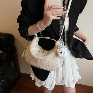 Detail view of woven beige crescent bag with zipper and cute plush charm on model
