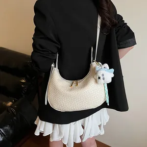 Detail of cream woven crescent bag featuring dual gold zippers and a plush star charm detail