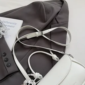 Gros plan du sac bandoulière blanc avec détail de nœud sur un blazer gris
