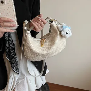 Detail of woven crescent bag featuring gold zipper, branded logo and decorative plush charm