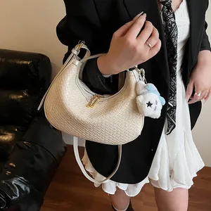 Detail of cream woven crescent bag with gold zipper and cute teddy bear charm