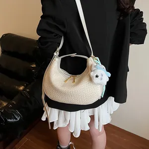 Close-up of cream woven crescent bag with textured faux leather and plush bear charm