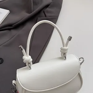 Détail d'un sac à main blanc avec poignée à nœud et finitions métalliques argentées