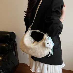 Chic cream woven crescent bag with plush bear charm worn as a stylish crossbody bag