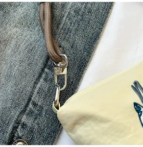 Close-up of beige fabric shoulder bag with embroidery and silver lobster clasp detail