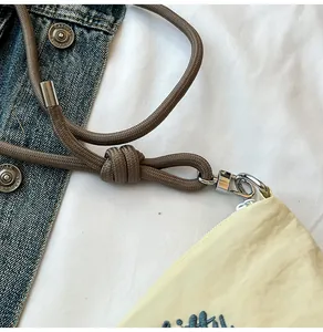 Close-up of yellow fabric bag featuring brown cord strap and blue embroidered text details