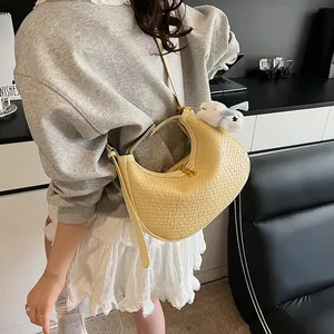 Detail of light yellow woven hobo bag featuring a plush doll charm and gold hardware