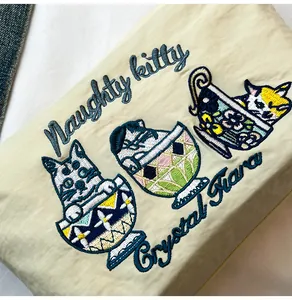 Close-up of vibrant cat embroidery on a beige fabric handbag with Naughty Kitty text