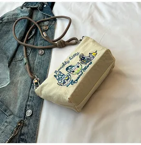 Detailed embroidery of naughty kitties on cream nylon crossbody bag with rope strap