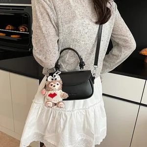 Détail du sac bandoulière en cuir noir avec charm ours en peluche dans un décor intérieur