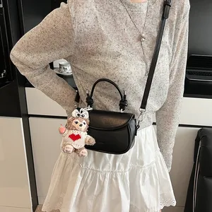 Détail du sac en cuir noir avec nœud métallique et pendentif ours en peluche doux