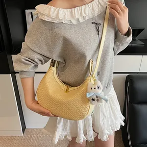 Detail of woven yellow hobo bag with gold fashion logo and cute plush charm pendant