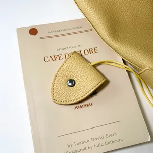 Close-up of yellow lychee grain leather keychain charm with silver snap button on a bag